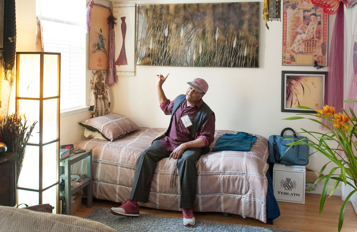 Man pointing to his apartment wall while sitting on a bed