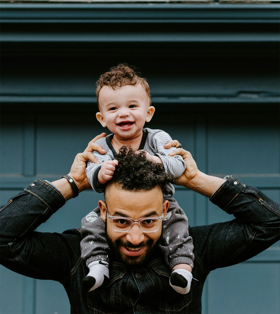 Man wearing glasses smiling holding smiling baby on shoulders